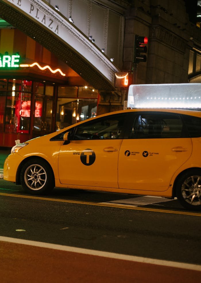 Modern yellow van taxi riding on street under bridge of Grand Central Terminal at night in New York