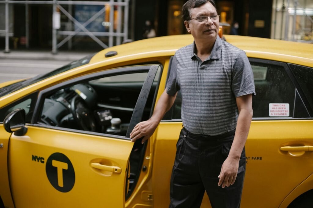Middle-aged male taxi driver standing by yellow cab in New York City street.