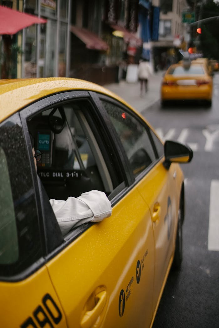 Services From above of unrecognizable person in white shirt sitting in modern yellow cab on asphalt roadway on urban background in town at daytime